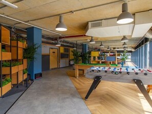 Un espacio interior moderno con una mesa de futbolín, estanterías de madera con plantas e iluminación colgante.