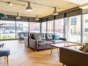 A modern lounge area with leather sofas and armchairs, large windows offering views of the street, and pendant lighting. - Cathedral Road by UTDM (Derby)