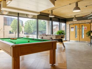 Una mesa de billar en una sala con ventanas amplias, una mesa de fútbol de mesa y una puerta de madera con un cartel.