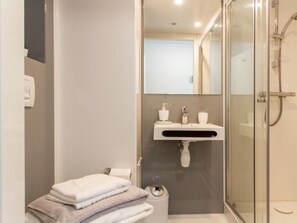 A modern bathroom with a glass shower enclosure, a white sink, and a stack of towels.