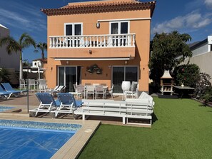 A two-story building with a balcony, outdoor seating, a swimming pool, and a well-maintained lawn. - South facing VILLA with Private Pool in tropical garden in Costa Adeje - Duque (Costa Adeje)