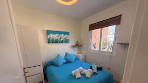 Une chambre à coucher comprenant un lit, des oreillers, une table de chevet, un tableau au mur, une fenêtre avec des stores et une porte.