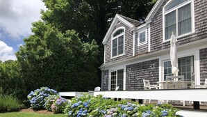 Une maison à deux étages avec une terrasse blanche et un jardin agrémenté de buissons d’hortensias.