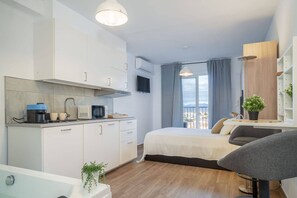 A modern hotel room with a kitchenette, a bed with a view, a desk, and a bathroom. - Studio with jacuzzi and sea view (Empuriabrava)