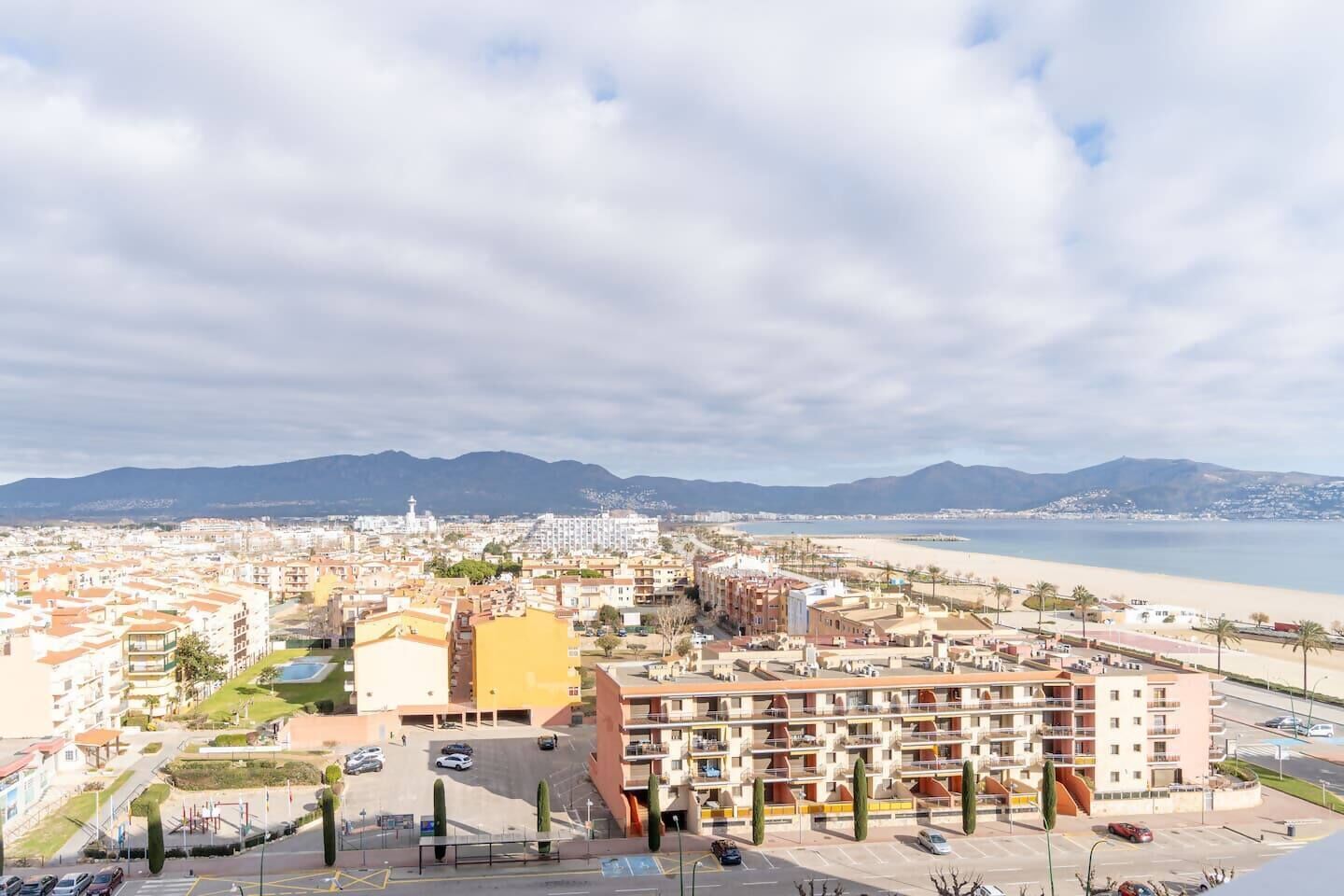 Un paysage urbain côtier avec un hôtel imposant à plusieurs étages, un parking et une plage en arrière-plan.
