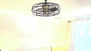 En snyggt bäddad säng med vita sängkläder och flera kuddar, ett sängbord med en lampa och en modern taklampa.