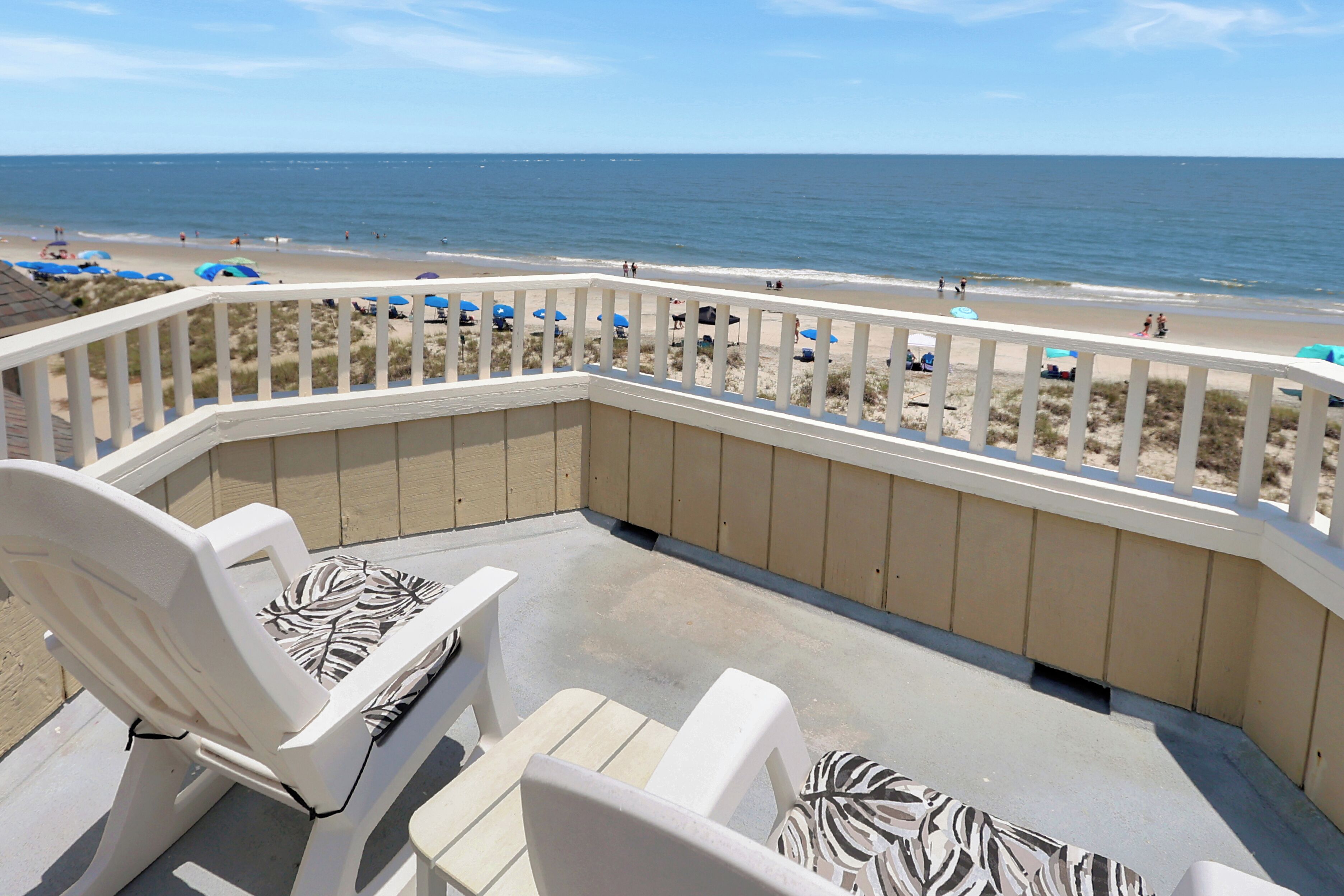 A balcony with white chairs and a view of the beach.