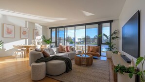 A modern living room with a sofa, coffee table, and TV. There are large windows and a view of the outdoors. - Waterfront Retreat-North Coogee, beachfront,Sauna, family friendly, Fremantle (North Coogee)