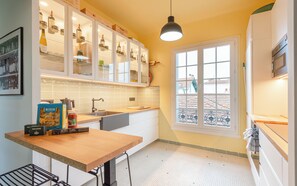 A kitchen with white cabinets, a wooden countertop, and a window with a view of buildings. - MISVA • KEYWEEK Architect-designed flat in Biarritz with garden (Biarritz)