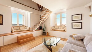 A modern living room with a glass coffee table, wooden staircase, and built-in seating along the windows. - EUGENIE - Apt with balcony and sea view and Hotel du Palais in Biarritz (Biarritz)