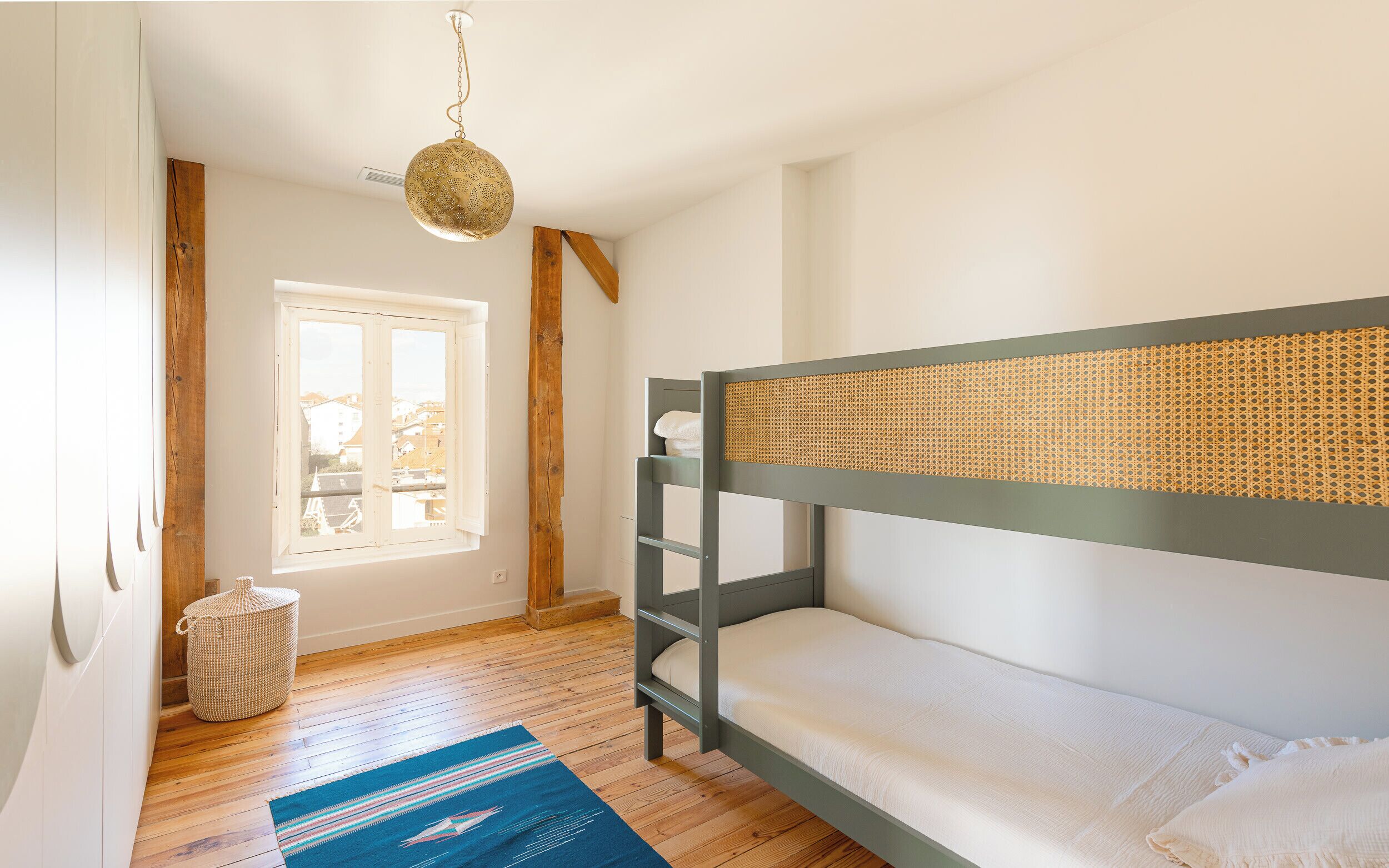 Habitación con literas, ventana, piso de madera y lámpara colgante.