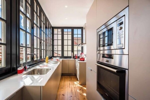 Een moderne keuken met een groot raam, roestvrijstalen apparatuur en een houten vloer.
