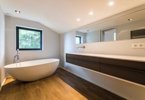 Un baño moderno con una bañera independiente, un espejo grande y un ventanal que proporciona luz natural.