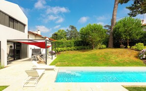 Una casa moderna con piscina, patio cubierto y césped cuidado.