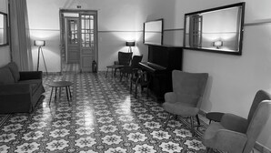 A room with patterned floor tiles, a sofa, a small table, two armchairs, a piano, and a mirror on the wall. - Tinion Urban Hotel (Tinos)