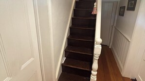 Una escalera con escalones de madera oscura y balaustres blancos, que lleva a un rellano con una puerta blanca.