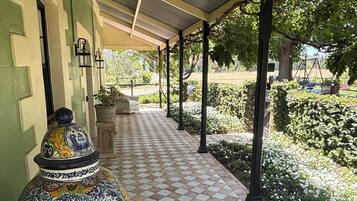 A covered walkway with a tiled floor, a decorative ceramic pot, and a garden area with white flowers and green shrubs.