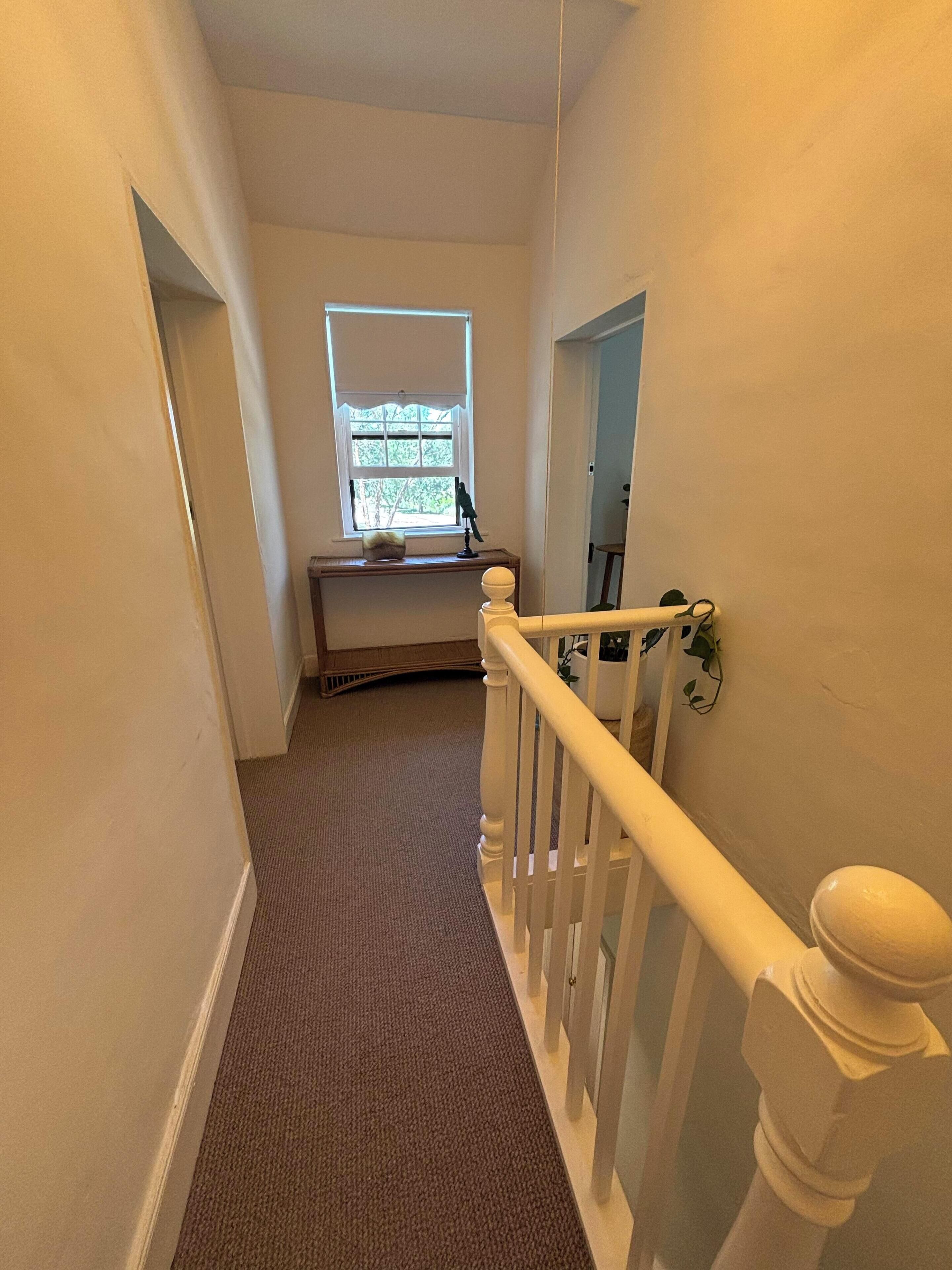 A carpeted staircase with white balusters and a handrail, leading to a landing with a window and a small table with a bird figurine.