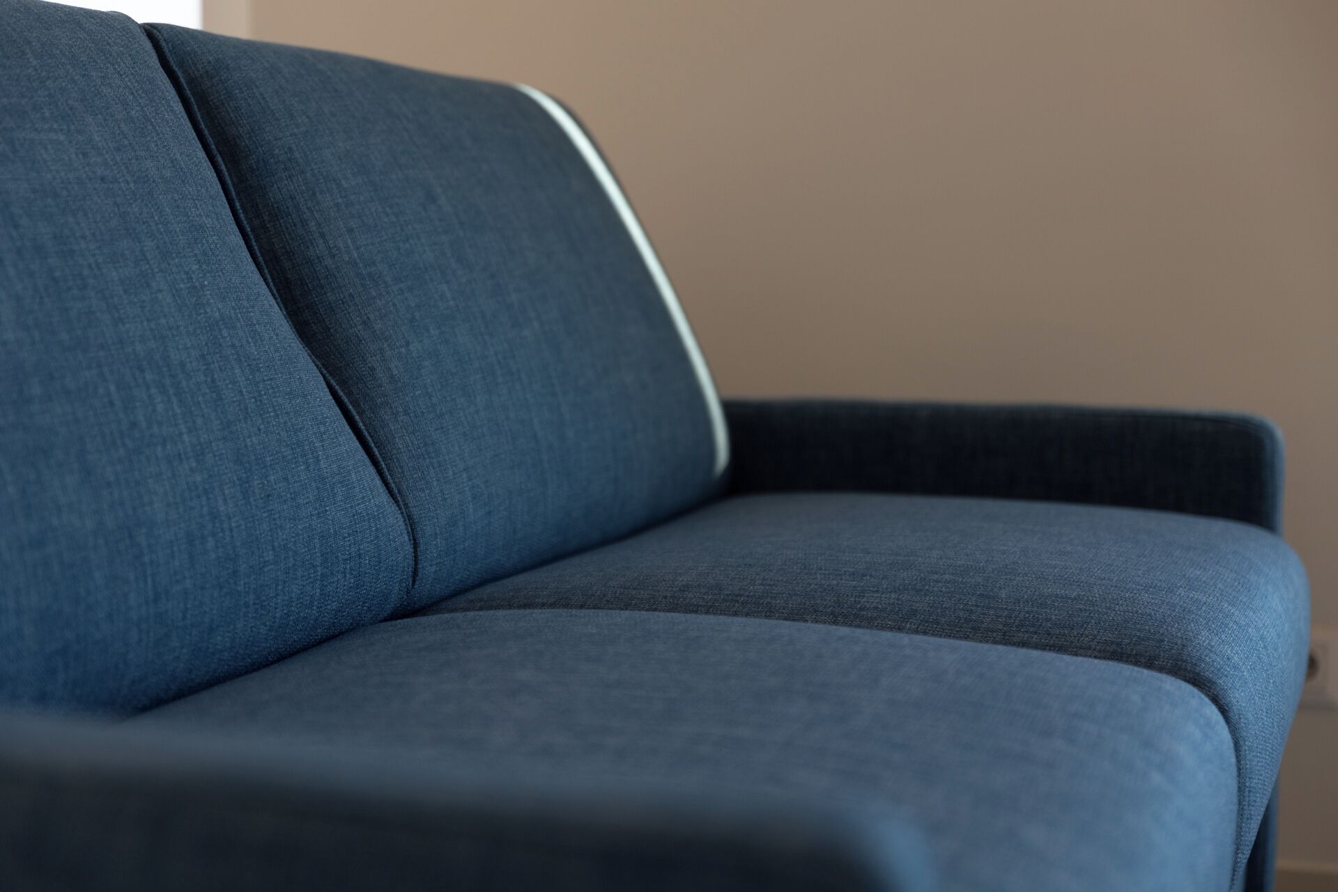 Primer plano de un sofá azul oscuro con textura suave y detalle de ribete blanco.