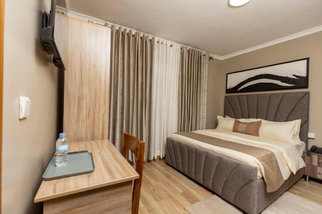 Une chambre d’hôtel avec un lit, un bureau, une chaise, une bouteille d’eau et un tableau au mur.