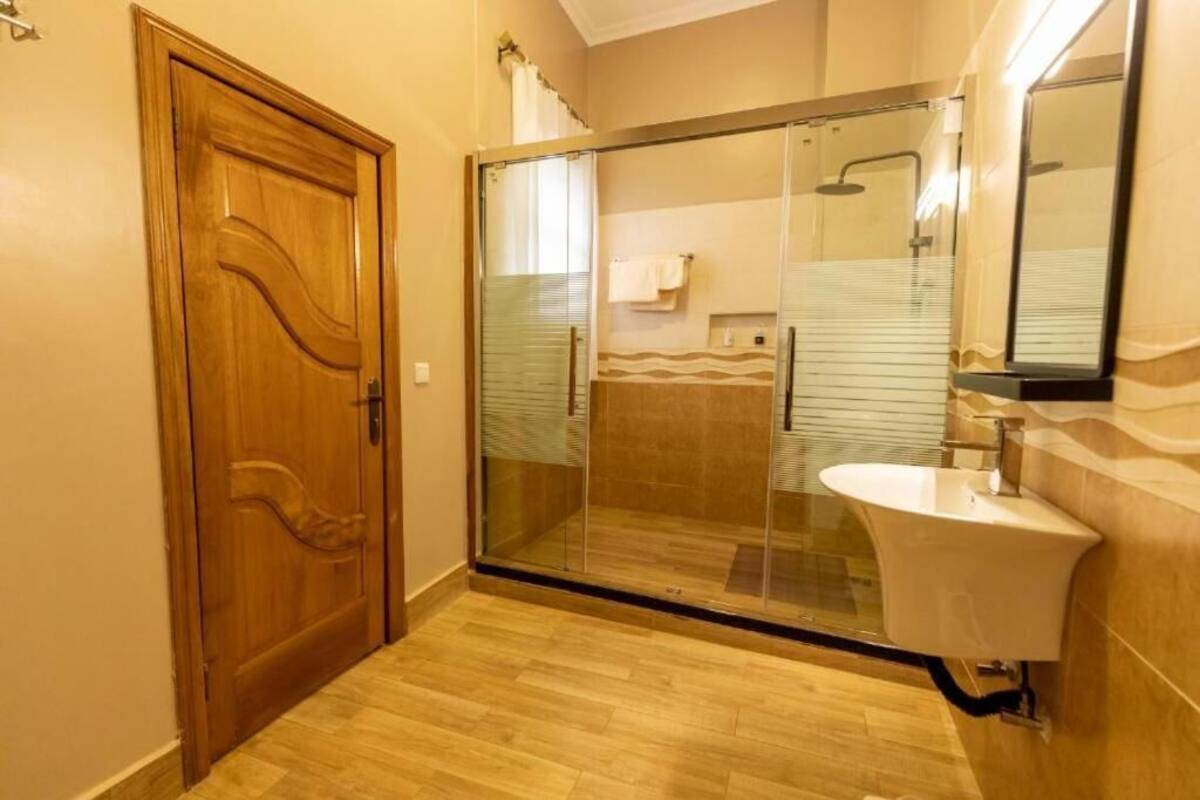 Un baño con puerta de madera, cabina de ducha de vidrio y lavamanos blanco.