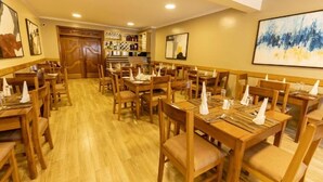 Un restaurante con mesas y sillas de madera, una zona de bar y obras de arte en las paredes.