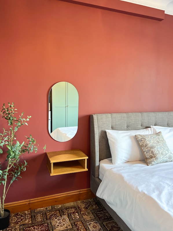 A bedroom with a bed, a nightstand, a mirror, and a potted plant.