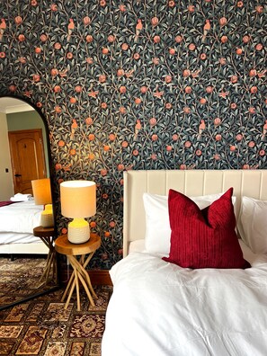 Una habitación de hotel con cama, mesita de noche con lámpara y un espejo grande.