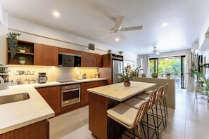 A modern kitchen with wooden cabinets, a central island, bar stools, and a large window providing natural light. - 1 BR Solana 1st Level Condo | Walk to Beach & Town (Huatulco)