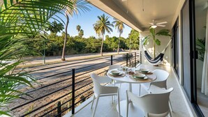 En balkon med et spisebord, der giver udsigt over et jernbanespor og palmer.