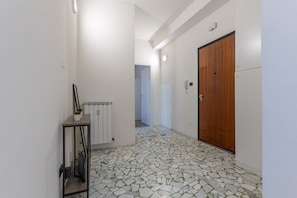 Un pasillo con suelo de baldosas, un radiador, una puerta de madera y una pequeña mesa con una planta.