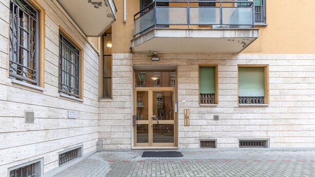 Un edificio con fachada de piedra, entrada por puerta de vidrio y un pequeño balcón con barandilla metálica.