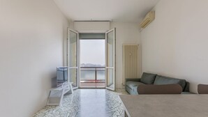 Una habitación moderna con piso de baldosas, un sofá, una mesa y vistas al balcón exterior a través de un vidrio.