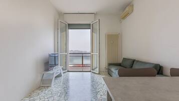 Une chambre moderne avec un sol carrelé, un canapé, une table et une vue sur un balcon extérieur, accessible par une porte vitrée.