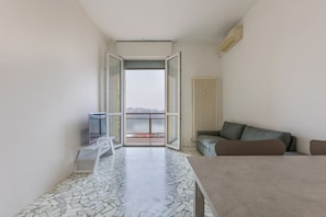 Una habitación moderna con piso de baldosas, un sofá, una mesa y vistas al balcón exterior a través de un vidrio.