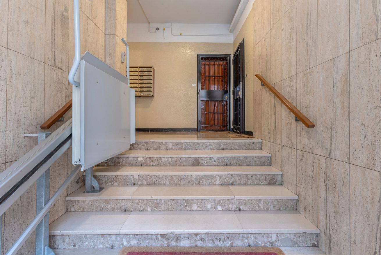 Una scala in marmo con ringhiere in metallo, una porta con cancello in metallo e un punto luce fissato al muro.