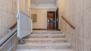 Un conjunto de escaleras de mármol con barandillas de metal, una puerta con reja metálica y una lámpara fijada a la pared.