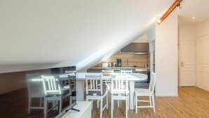 A modern kitchen with white cabinetry, a dining area with white chairs, and a wooden floor. - Le  Joseph - Appartement au calme (Annecy)