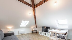 A modern loft apartment with exposed wooden beams, a loft bed, a dining area with a table and chairs, a TV, and skylights. - Le  Joseph - Appartement au calme (Annecy)