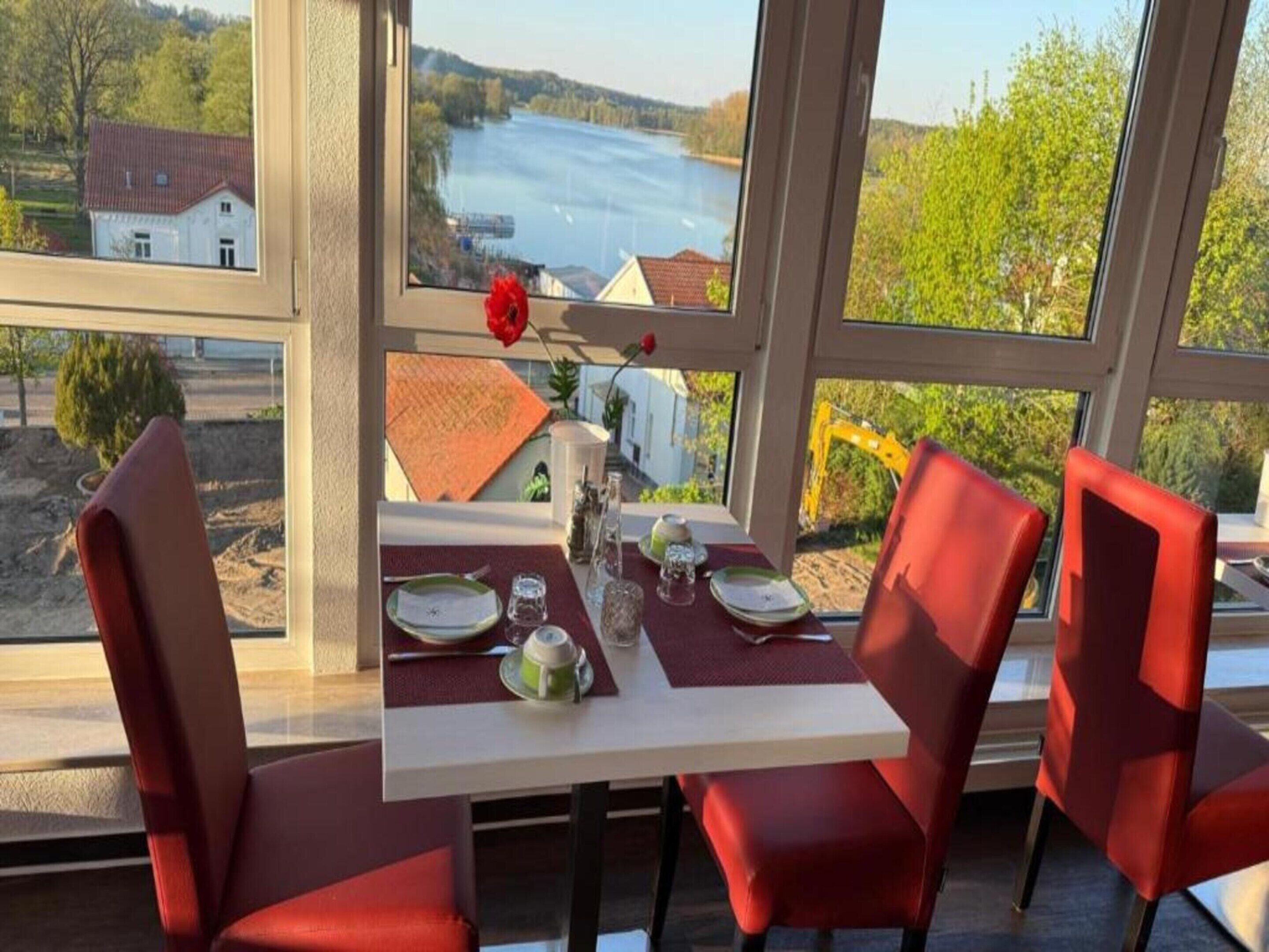 A dining area with a table set for four, large windows offering a view of a river and greenery.