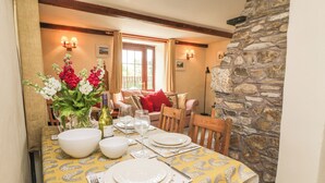 A dining area with a table set for four, a stone wall, and a cozy seating area with a sofa and cushions. - Applestore (Wadebridge)