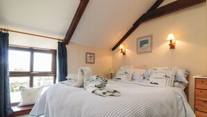 A bedroom with a large bed, a window with curtains, a wooden dresser, and two wall-mounted lamps. - Applestore (Wadebridge)
