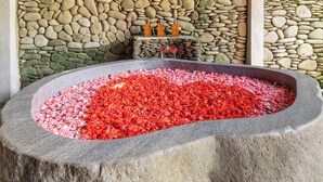 A stone wall with a stone basin filled with red flowers, a shelf with bottles, and a stone pillar. - Saughina Ubud Tranquil Ubud Villa With Private Infinity Pool and Jungle Views (Ubud)