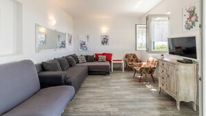 Een moderne woonkamer met een hoekbank, een rode fauteuil, een bijzettafeltje, een televisie en een kast.