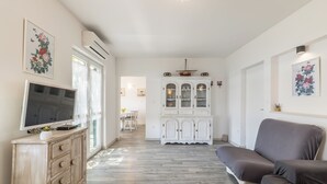 Een woonkamer met een televisie, een bank, een kast en een eethoek op de achtergrond.