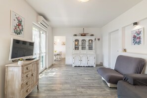 A living room with a TV, a sofa, a cabinet, and a dining area in the background. - Domus Alta, Two-bedroom House in Podgora (Podgora)