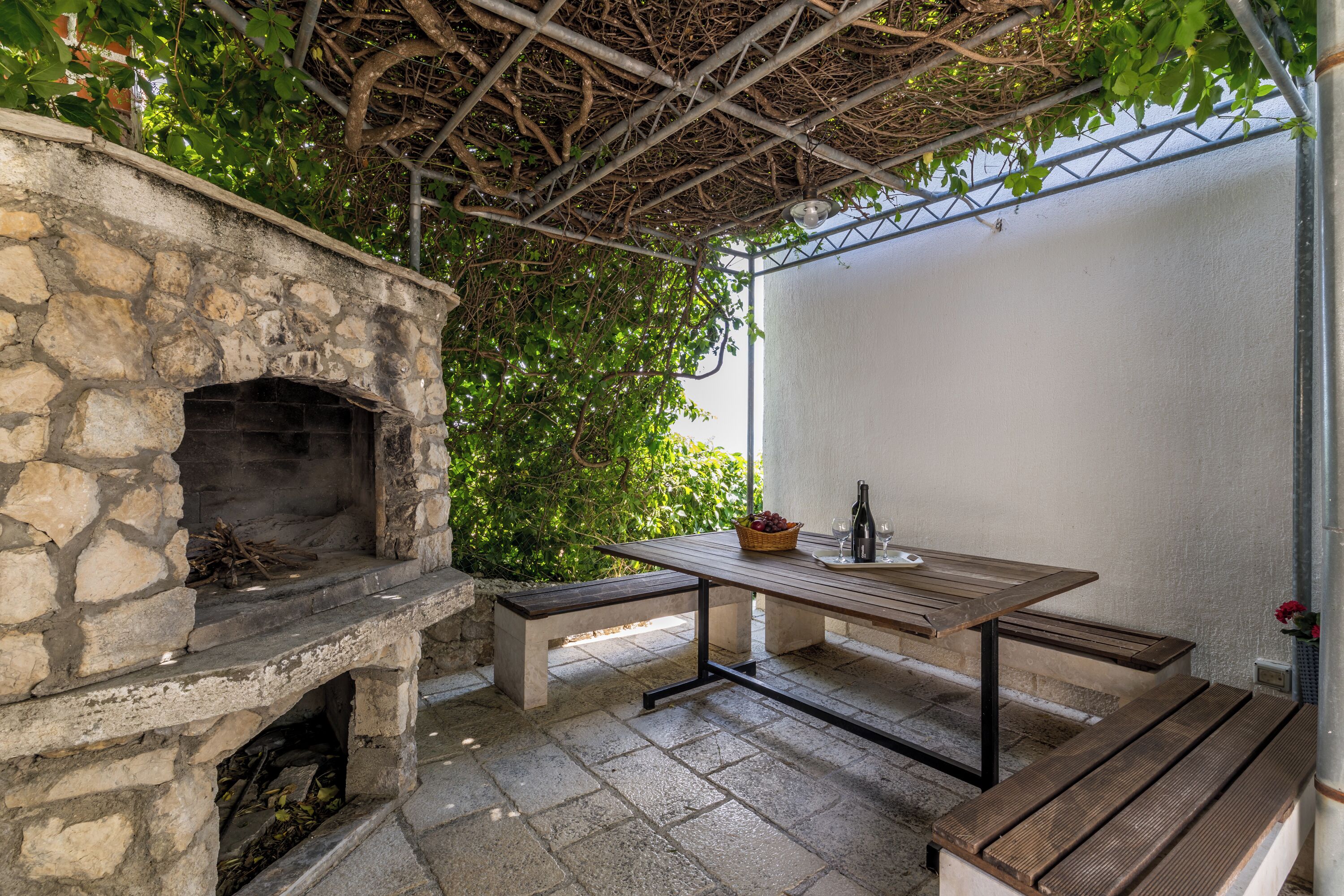 A stone-built outdoor kitchen with a built-in oven, a wooden table, and benches.