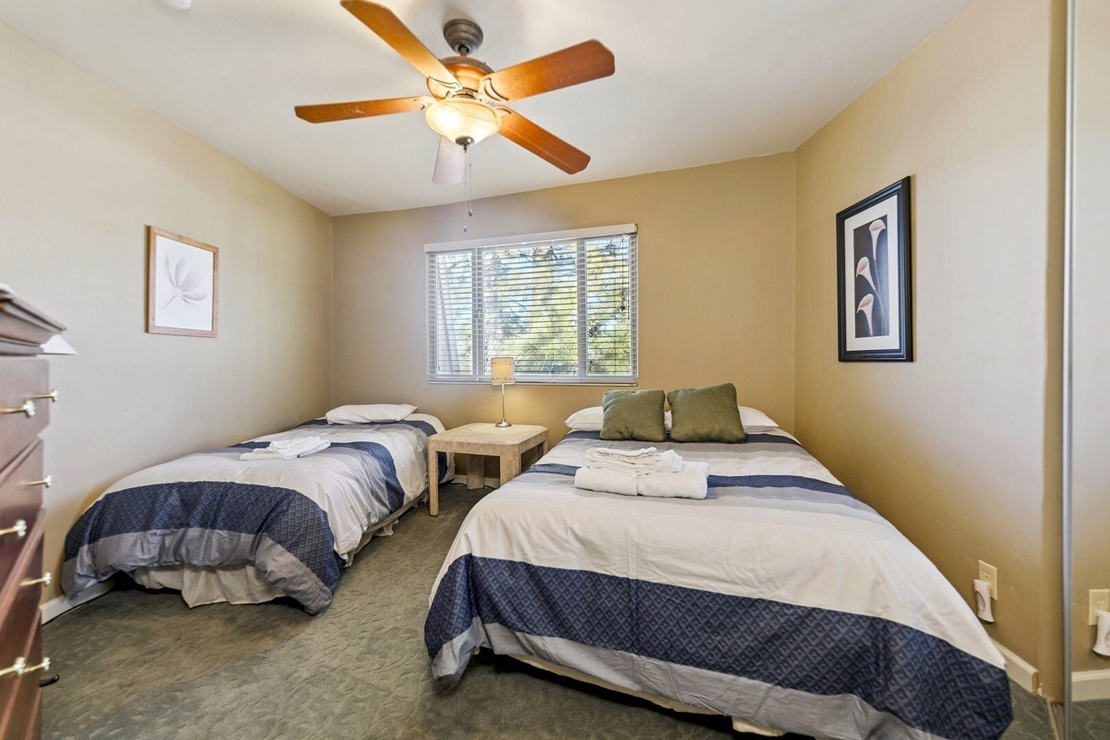 A hotel room with two beds, a ceiling fan, a window with blinds, and a dresser.