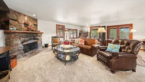 A cozy living room with a stone fireplace, leather sofa, and a coffee table. - Twin Fawns 2 Bedroom Cabin (Estes Park)