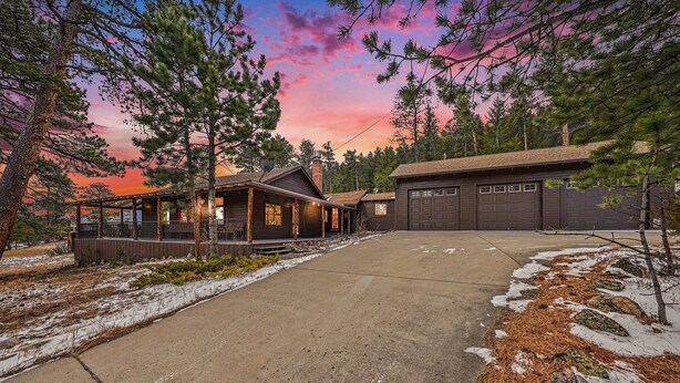 A cabin with a covered porch, a garage, and a driveway leading to the entrance. - Twin Fawns 2 Bedroom Cabin (Estes Park)